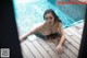 A woman in a blue bikini laying on a wooden deck next to a pool.