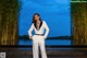 A woman in a white suit standing in front of a pond.